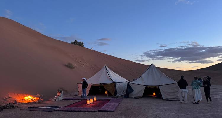 Traditional canvas tents glow with lantern light against towering sand dunes at dusk.