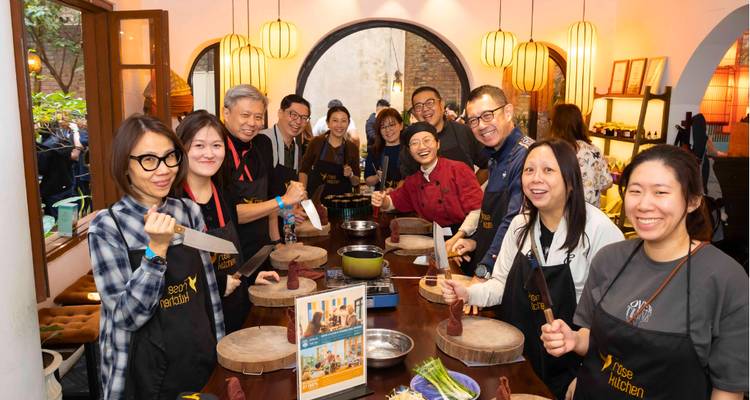 Foto grupal de personas con cortadores de cocina e ingredientes en una cocina.