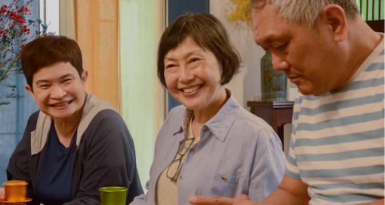 Tres personas sentadas alrededor de una mesa, sonriendo y hablando.
