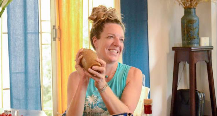Mujer sentada en una mesa sosteniendo una papa, sonriendo.