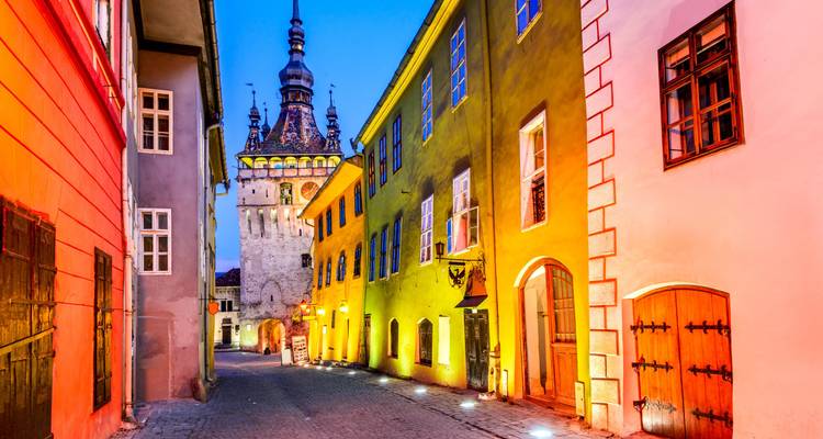 Rue historique colorée avec une haute tour d'horloge à Sighișoara au crépuscule.
