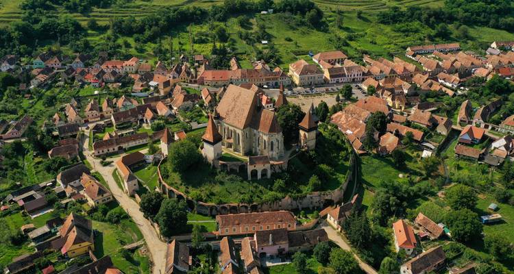 Vue aérienne d'une église fortifiée à Biertan entourée de champs et de verdure.