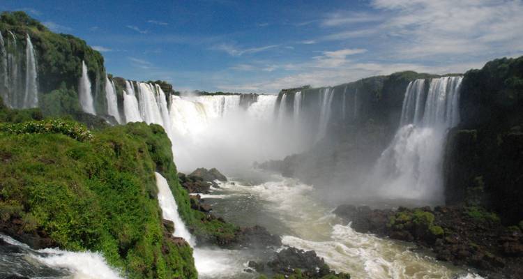 Ein Panoramablick auf die Iguazu-Wasserfälle mit herabstürzendem Wasser und üppigem Grün.