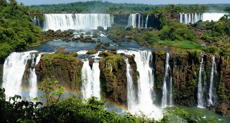 Ein lebendiger Blick auf die Iguazú-Fälle mit Wasserfällen und einem Regenbogen.