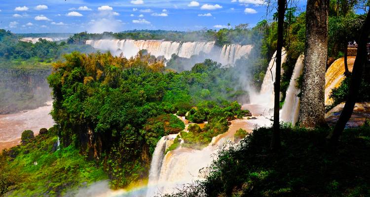 Eine grüne Szenerie der Iguazu-Fälle mit mehreren Wasserfällen und einem sichtbaren Regenbogen.