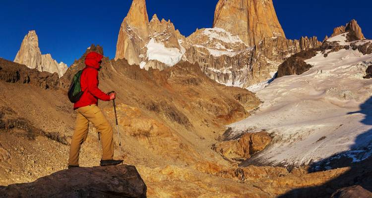 Personne en veste rouge faisant de la randonnée vers des montagnes enneigées.