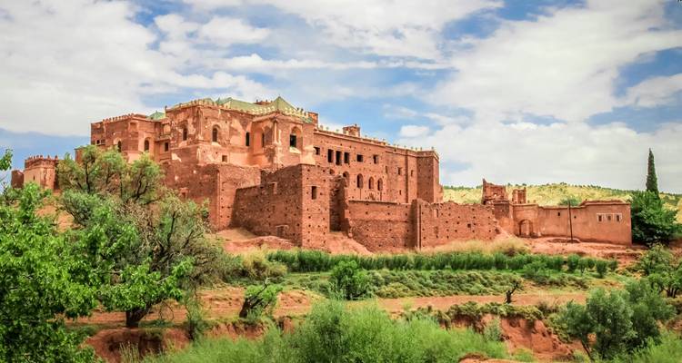 Forteresse historique en adobe sur une colline verte sous un ciel partiellement nuageux.