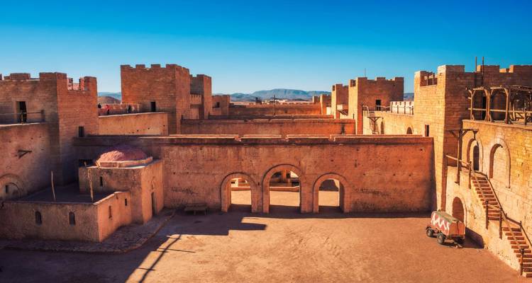 Ancienne forteresse de pierre avec arches et tour dans un paysage désertique.