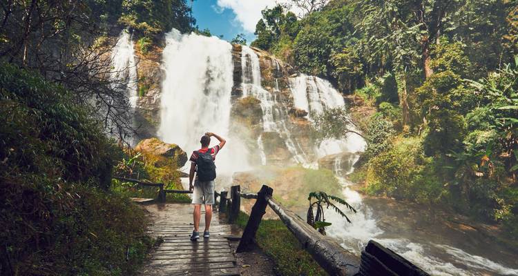 Ein Wanderer, der vor einem Wasserfall steht und die Aussicht genießt.