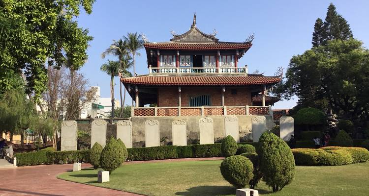 Bâtiment traditionnel entouré de verdure et de statues.
