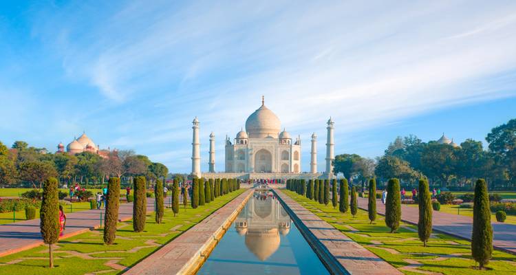 Le Taj Mahal avec un bassin réfléchissant limpide et des jardins vibrants sous un ciel bleu.