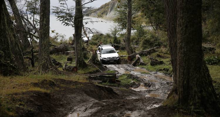 Un véhicule tout-terrain robuste sur un sentier boueux en forêt près d'un lac.
