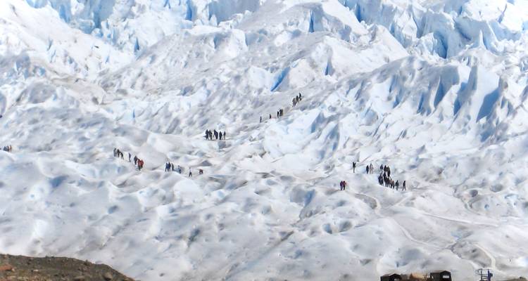 Des gens faisant de la randonnée sur une vaste surface glaciaire gelée.