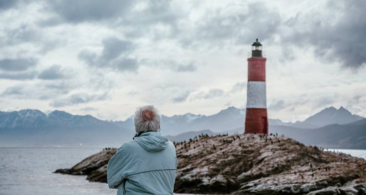 Personne regardant vers un phare sur une île rocheuse.