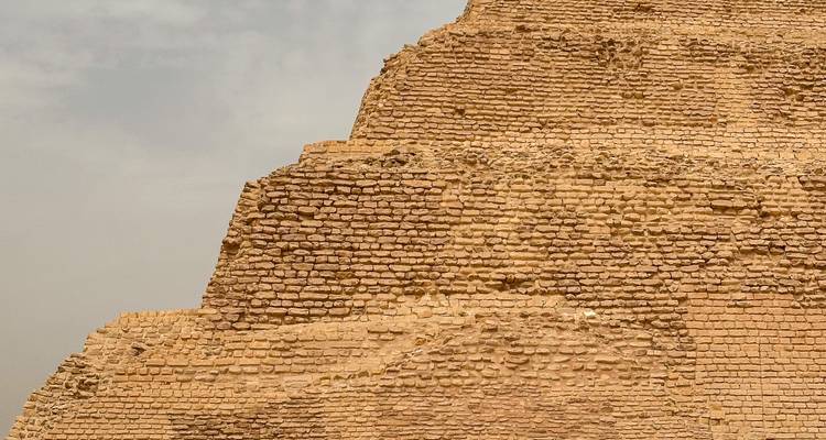 Gros plan de blocs de calcaire anciens formant la pyramide à degrés de Saqqarah sous un ciel brumeux.