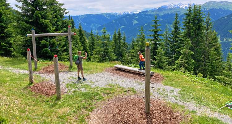 Un niño jugando en un parque infantil natural en las montañas mientras un adulto observa.