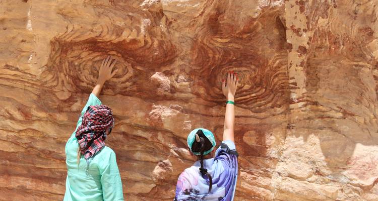 Deux voyageurs touchent des motifs colorés et tourbillonnants de grès sur une paroi rocheuse à Pétra.
