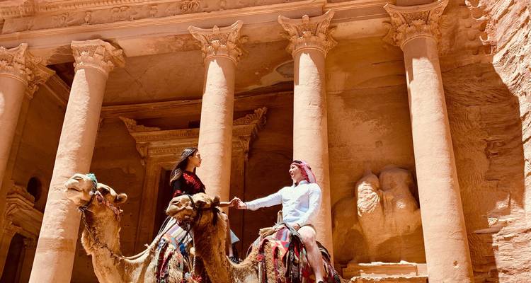 Un homme et une femme sur des chameaux devant l'emblématique Trésor de Pétra avec ses imposantes colonnes de grès.