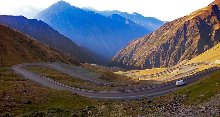 Route de montagne sinueuse avec un véhicule et un paysage montagneux époustouflant.