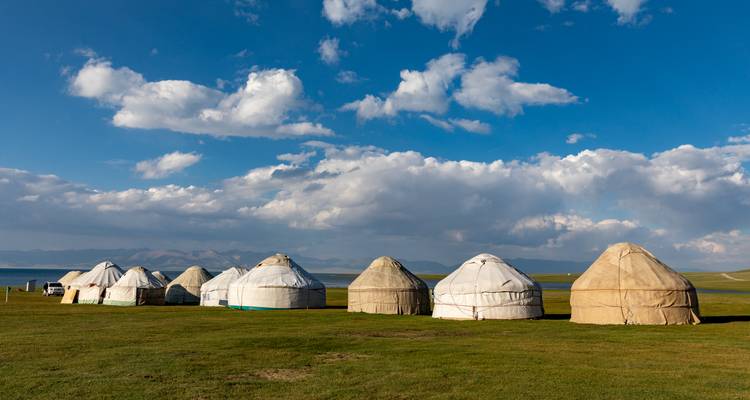 Yourtes installées sur une prairie verte avec un ciel bleu et des nuages.