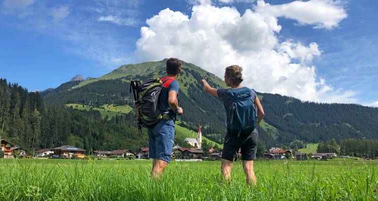 Deux randonneurs dans une zone herbeuse avec des montagnes en arrière-plan.