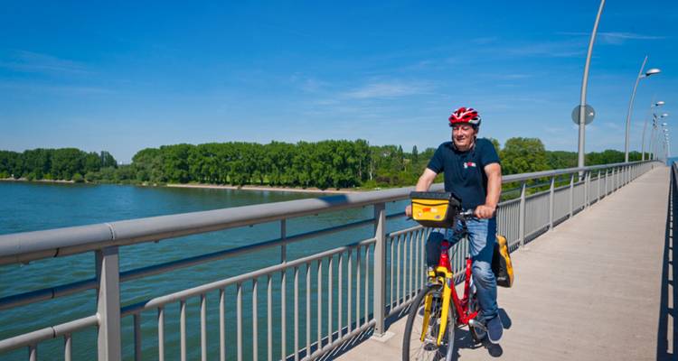 Homme faisant du vélo sur un pont au-dessus d'une rivière par une journée ensoleillée.
