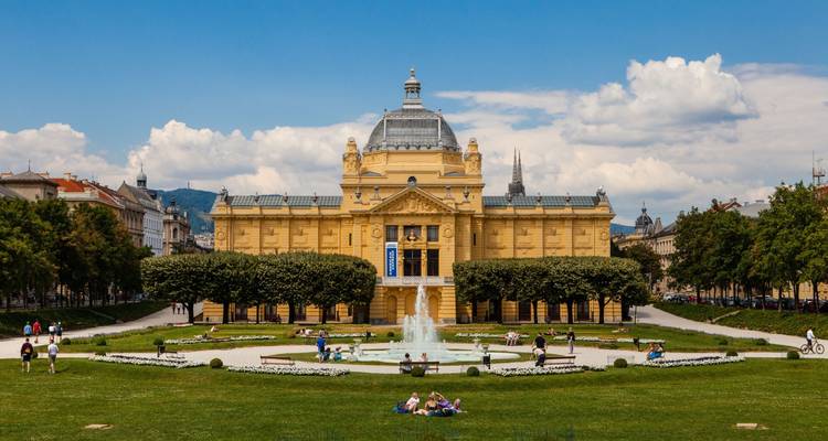 Bâtiment historique orné avec une fontaine et des gens qui se détendent dans un parc.