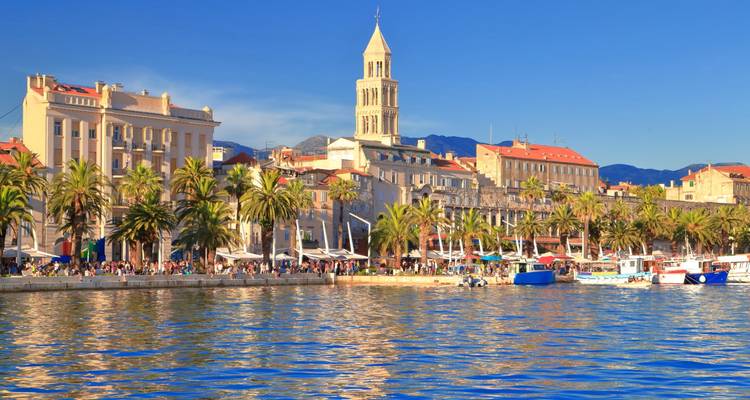 Promenade au bord de l'eau avec bâtiments historiques et palmiers.