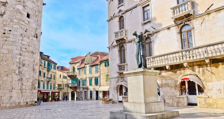 Place de ville avec de vieux bâtiments en pierre et une statue.