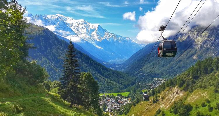Téléphériques gravissant une vallée verdoyante avec des sommets montagneux.