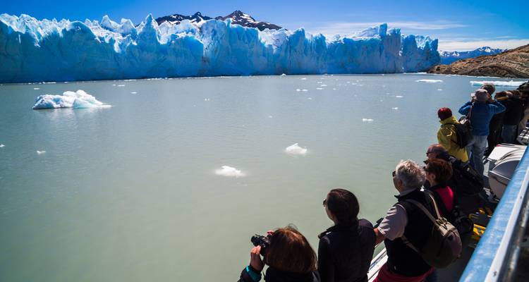Des touristes prenant des photos d'un glacier depuis un bateau.