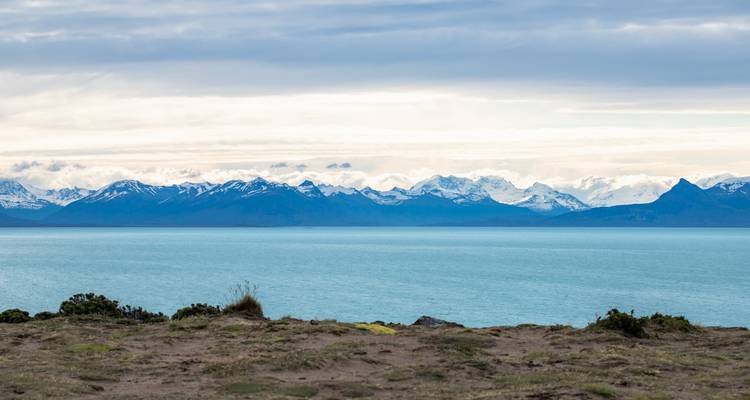 Vue d'un grand lac avec une chaîne de montagnes au loin sous un ciel nuageux.
