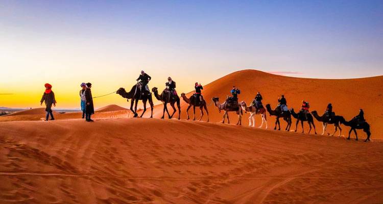 Grupo de personas montando camellos en las dunas de arena al atardecer en Merzouga, Marruecos.