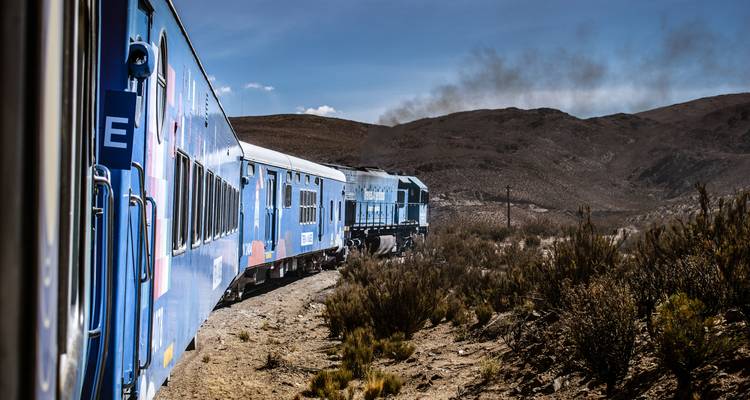 Un train bleu traversant un paysage montagneux et aride.