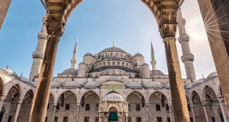 Vue de la cour intérieure du grand de la Mosquée Bleue encadrée par des arcs en pierre sous un ciel bleu dégagé.