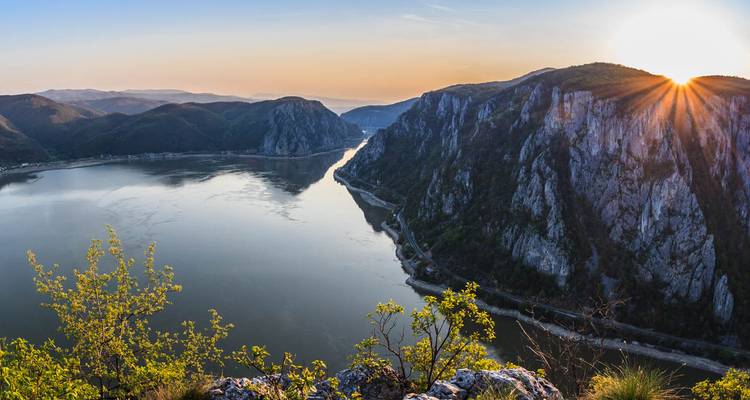 Zon die over de steile kliffen van de IJzeren Poort-kloof gluurt met de kalme Donau eronder.