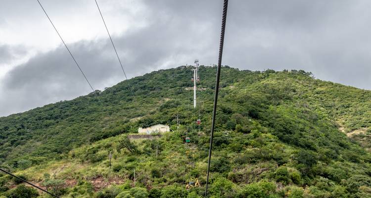 Un téléphérique qui monte une colline verte avec un ciel nuageux.
