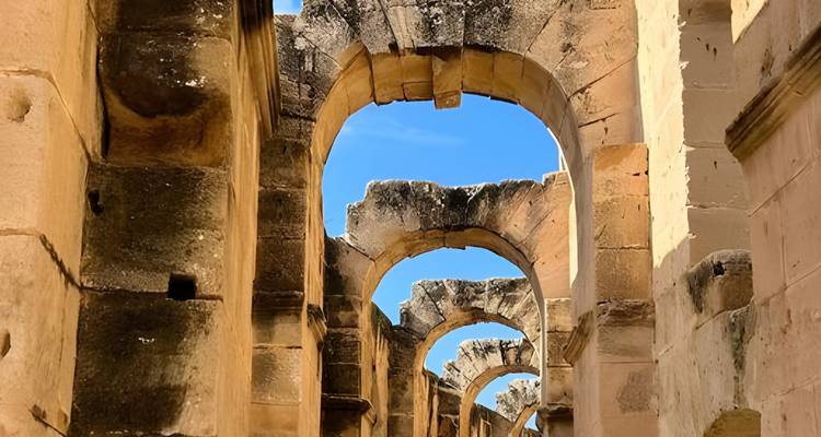 Anciennes arches de pierre en ruines contre un ciel bleu.