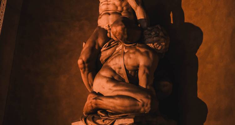 Escultura de mármol dramáticamente iluminada de figuras musculosas en un oscuro ambiente de museo interior.
