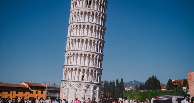 La Torre Inclinada de Pisa inclinándose contra un cielo azul despejado con multitudes de turistas en su base.