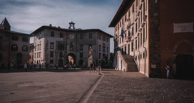 Plaza amplia rodeada de edificios italianos históricos con gente paseando y reuniéndose en la luz del atardecer.