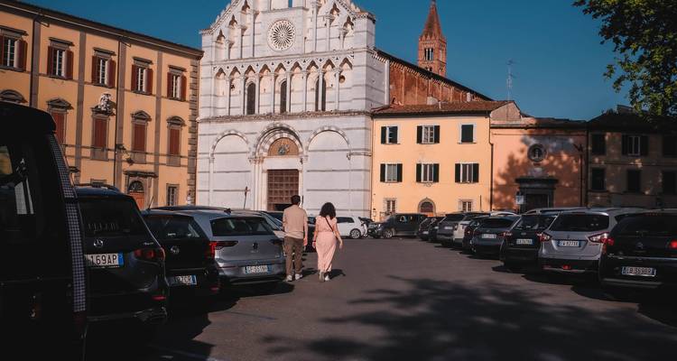 Una pareja caminando a través de un estacionamiento hacia una iglesia de fachada blanca con un campanario alto.
