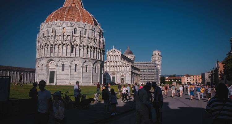 Vista del Baptisterio de Pisa, la Catedral y la Torre Inclinada con turistas caminando por el sendero.