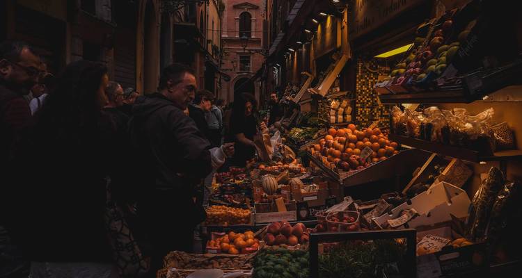 Mercado de comida en un callejón con poca luz donde los locales compran frutas frescas y coloridas y otros productos.