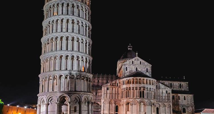 Torre Inclinada iluminada y Catedral de Pisa dramáticamente iluminadas contra el cielo nocturno negro.