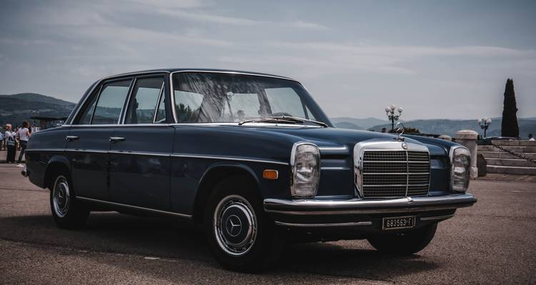 Classic blue Mercedes sedan parked at a scenic lookout with hills under hazy skies