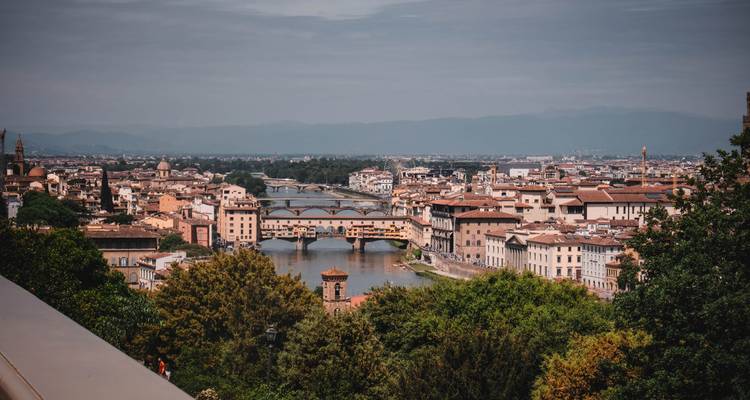 Elevated view of the Arno River with multiple bridges including the Ponte Vecchio framed by greenery