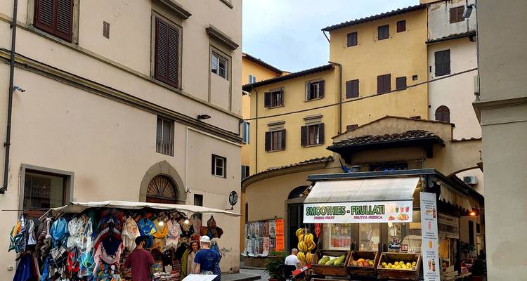 Small square with market stalls selling hats, scarves and fresh smoothies between pastel buildings