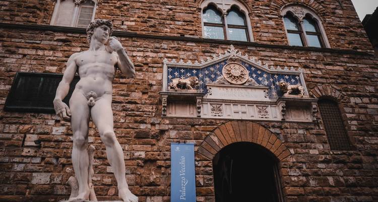 Marble replica of Michelangelo’s David standing before the ornate entrance of Palazzo Vecchio