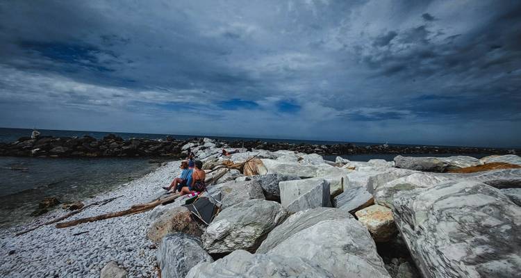 Rocky seashore with people relaxing on white stones under a dramatic cloudy sky